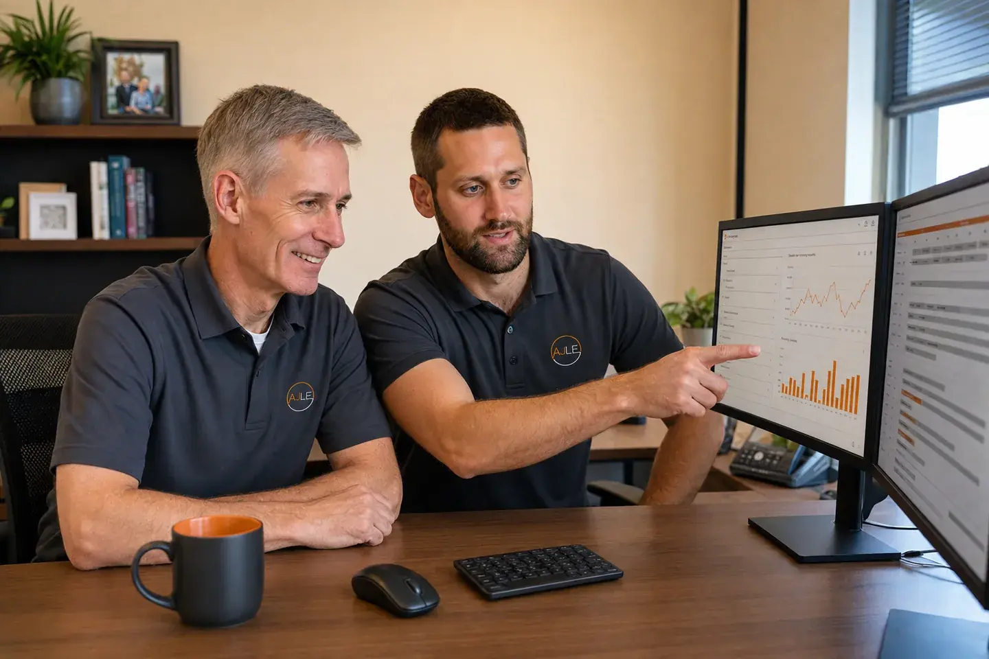 Illustrated scene of John and Matt together in their office, with Matt pointing to a dashboard on one of two computer screens as John follows along
